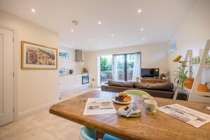 A modern kitchen with white cabinets, a dining table with breakfast items, a sofa, and a TV in the living area.