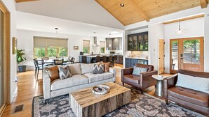 A spacious living area with a high ceiling, wooden beams, a sofa, a coffee table, and a dining area with chairs and a table.