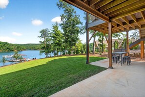 A covered patio with a view of a lake, a grassy lawn, and a dock with a boat. - Dockside of the Moon | Lakefront Luxury, Views & Private Dock (Nebo)