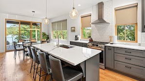 A modern kitchen with a large island, bar stools, a stove, and a view of the outdoors.