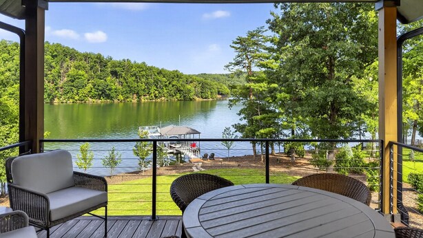 A covered outdoor area with a view of a lake, wicker furniture, and a small dock.