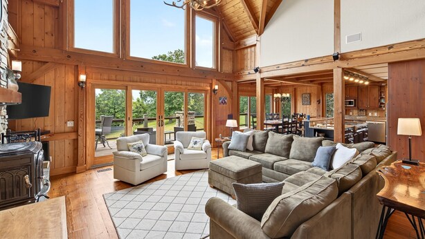 A spacious living area with wooden beams, large windows, and a fireplace. - Windy Path Farm | Animals, Hot Tub, Game Room + Breathtaking VIEWS! (Fairview)