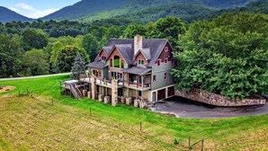 A large, multi-story house with a stone foundation, a front porch, and a garage. - Windy Path Farm | Animals, Hot Tub, Game Room + Breathtaking VIEWS! (Fairview)