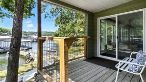 A covered deck with a wooden railing, a white chair, and a view of a lake with boats. - Lakefront Home w/ Dock, Boat Slip, Private Ramp, Kayaks, Paddle Boards & Firepit (Sunrise Beach)