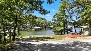 A lakeside property with a paved driveway, dock, and boats. - Lakefront Home w/ Dock, Boat Slip, Private Ramp, Kayaks, Paddle Boards & Firepit (Sunrise Beach)