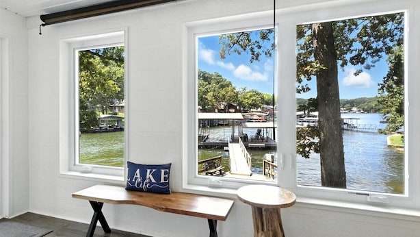 A room with three large windows overlooking a lake, a bench, and a small round table. - Lakefront Home w/ Dock, Boat Slip, Private Ramp, Kayaks, Paddle Boards & Firepit (Sunrise Beach)