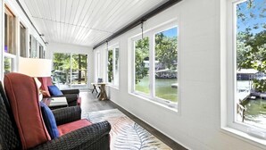 A sunlit room with large windows overlooking a water body, wicker furniture, and a small table with a lamp. - Lakefront Home w/ Dock, Boat Slip, Private Ramp, Kayaks, Paddle Boards & Firepit (Sunrise Beach)