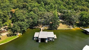 A lakeside cabin with a dock and a small boat. - Lakefront Home w/ Dock, Boat Slip, Private Ramp, Kayaks, Paddle Boards & Firepit (Sunrise Beach)