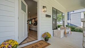 A modern house entrance with a 'COME IN' mat, a wooden bench, and potted plants.