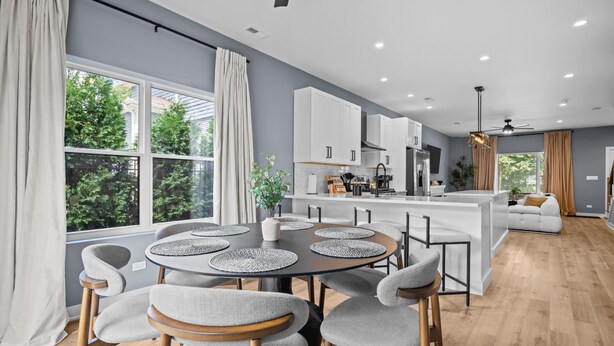 A modern kitchen with white cabinets, a central island, and a dining area with a round table and chairs.