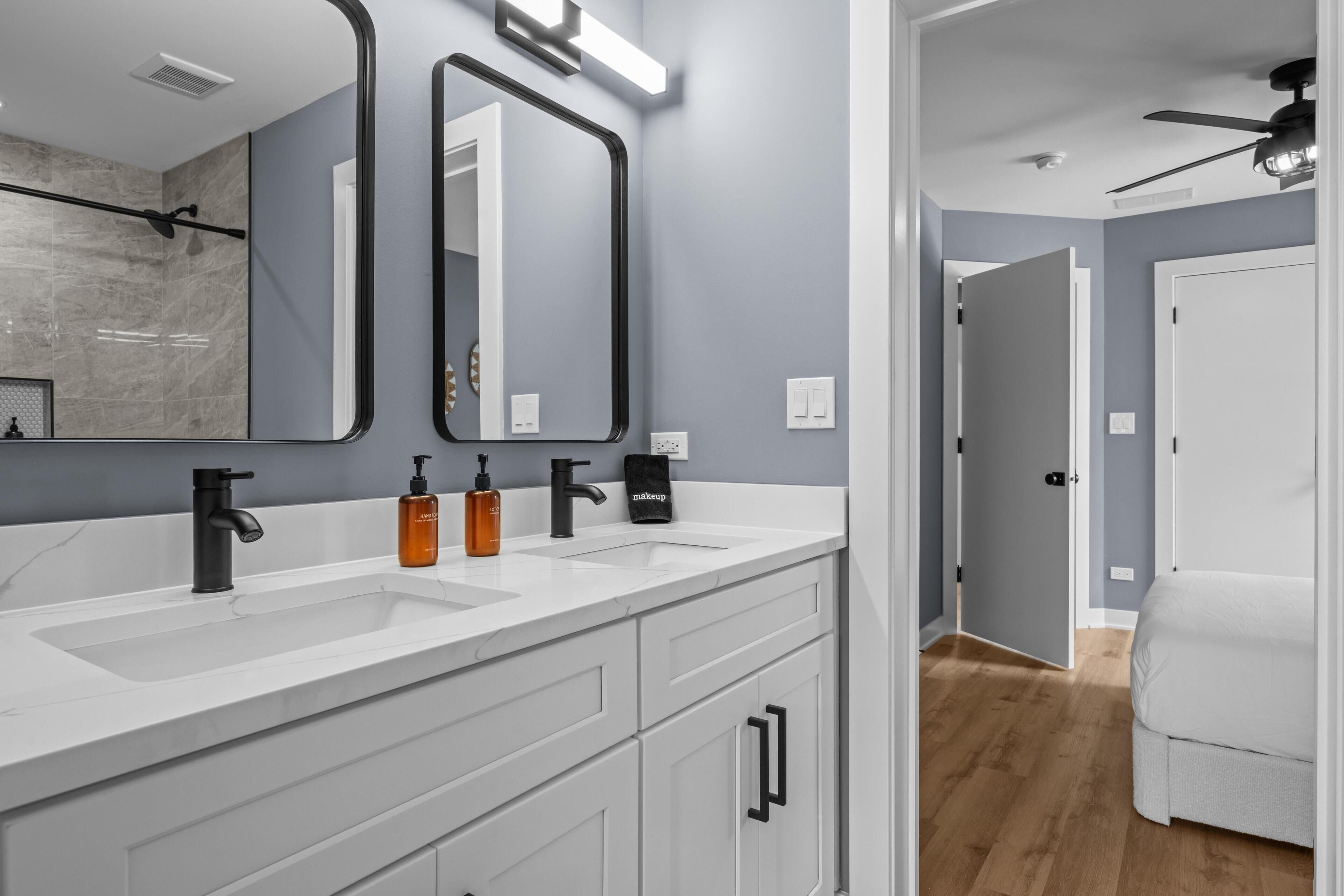 Un baño moderno con tocador blanco, dos lavamanos, grifos negros y un espejo grande.