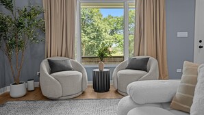 A modern living room with two plush armchairs, a small side table, and a large window with curtains.