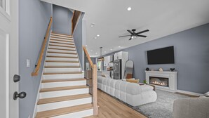 A modern living room with a staircase, a fireplace, and a television mounted on the wall.