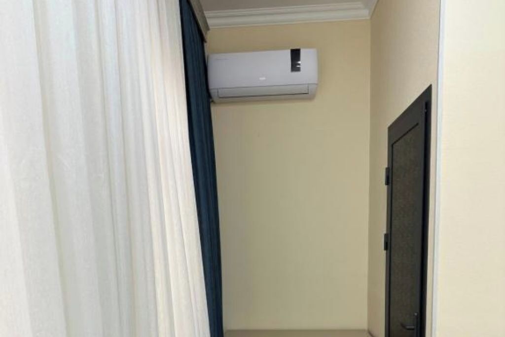 A narrow hallway with a white air conditioning unit mounted on the wall and a door at the end.