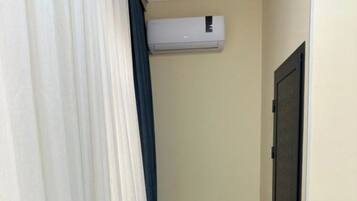 A narrow hallway with a white air conditioning unit mounted on the wall and a door at the end.