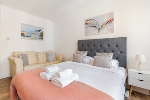 Una habitación de hotel con cama, sofá, mesita de noche y un cuadro en la pared.
