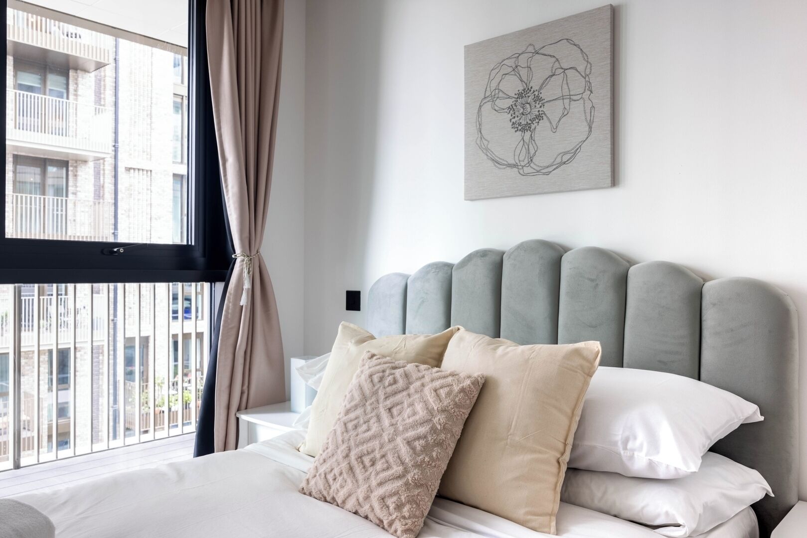 Un dormitorio con cama, cabecera y ventana con cortinas.