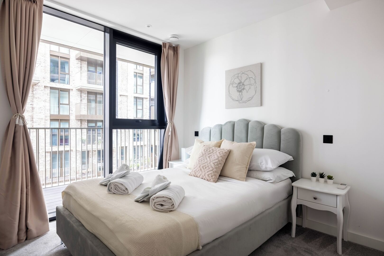 Une chambre d’hôtel avec un grand lit, une table de chevet, une œuvre d’art accrochée au mur et une vue sur le balcon extérieur.