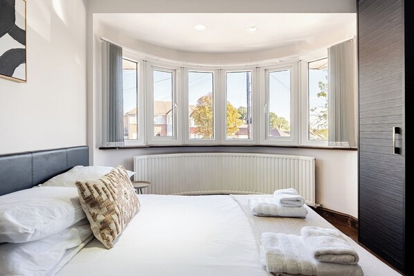 Un dormitorio con una cama grande, un radiador y un ventanal con cortinas.