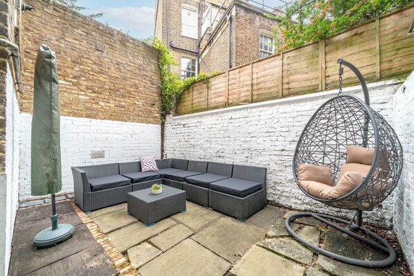 Un patio con un sofá modular, un sillón colgante redondo y una mesita.