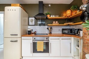 Une cuisine compacte avec un réfrigérateur blanc, une cuisinière, un four à micro-ondes et un grille-pain. Des étagères en bois, situées au-dessus du plan de travail, servent à ranger divers ustensiles de cuisine.