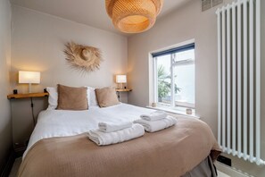 A hotel room with a bed, bedside lamps, a window with a view, and a radiator.