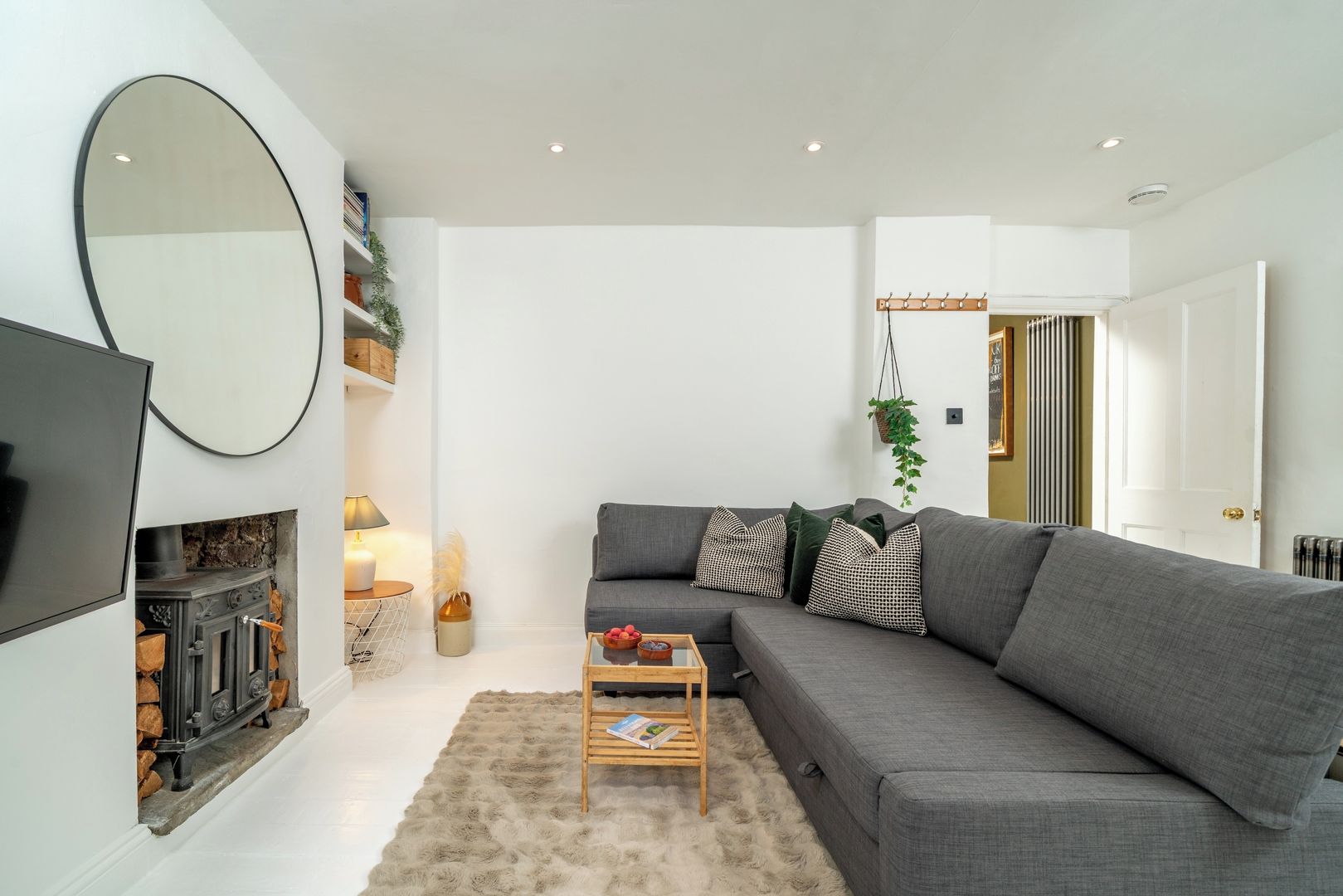 A modern living room with a grey sofa, a fireplace, a television, and a large mirror.