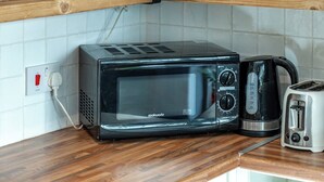 A kitchen with a microwave, toaster, and a hanging light fixture. - Cozy Nook • Wood Burner • Terrace (London)