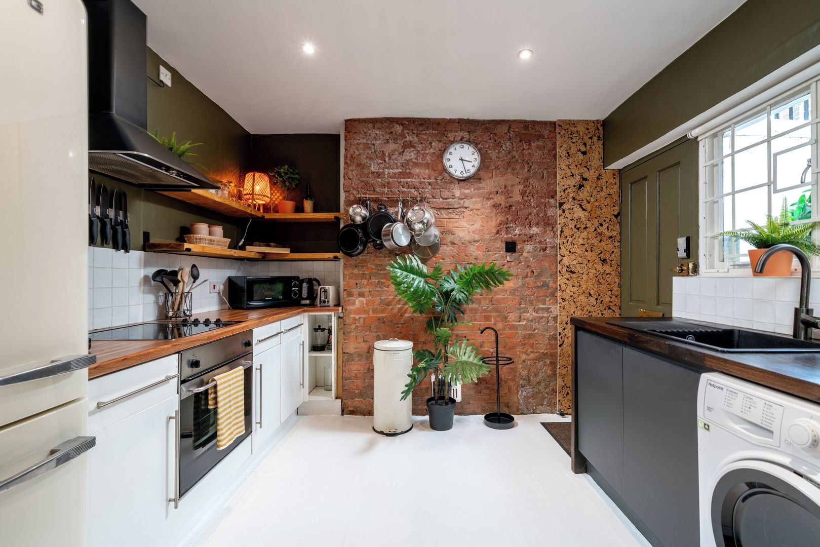 A modern kitchen with a brick wall, a clock, and a washing machine.