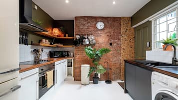 A modern kitchen with a brick wall, a clock, and a washing machine.