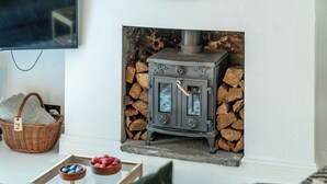 A living room with a stone fireplace, a television mounted on the wall, a wicker basket, and a tray with fruits. - Cozy Nook • Wood Burner • Terrace (London)