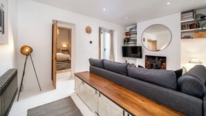 A modern living room with a sofa, a coffee table, a TV, and a fireplace. - Cozy Nook • Wood Burner • Terrace (London)