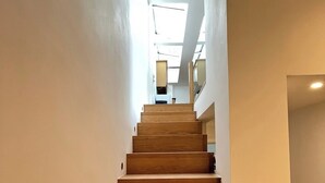Un escalier avec des marches en bois menant vers le haut, des murs blancs et une lucarne au sommet.
