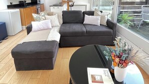 Un salon moderne avec un canapé gris foncé, un pouf assorti et une table basse ronde noire sur laquelle reposent un livre et un vase de fleurs.