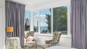 A bedroom with a large window, two armchairs, a bedside table with a lamp, and a bed with striped bedding. - Greenbank, Holiday Property Dale, Sleeps 6, 3 bedrooms,  bathrooms (Haverfordwest)