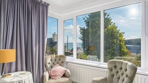 A room with two armchairs, a table with a floral tablecloth, and a view of a body of water through large windows. - Greenbank, Holiday Property Dale, Sleeps 6, 3 bedrooms,  bathrooms (Haverfordwest)