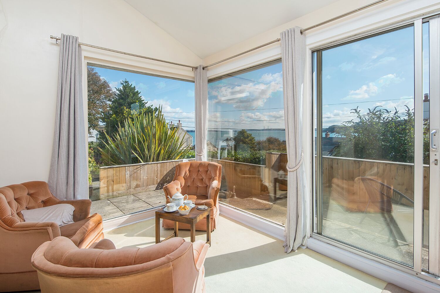 A spacious balcony with a seating area, large windows, and a view of greenery and buildings.