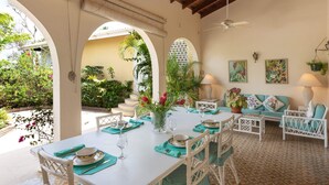 A dining area with a table set for four, surrounded by white wicker chairs. There are potted plants and a sofa with teal cushions. - Villa Casabella | Ocean View - Located in  Fabulous Saint James with Private Pool (Saint James)