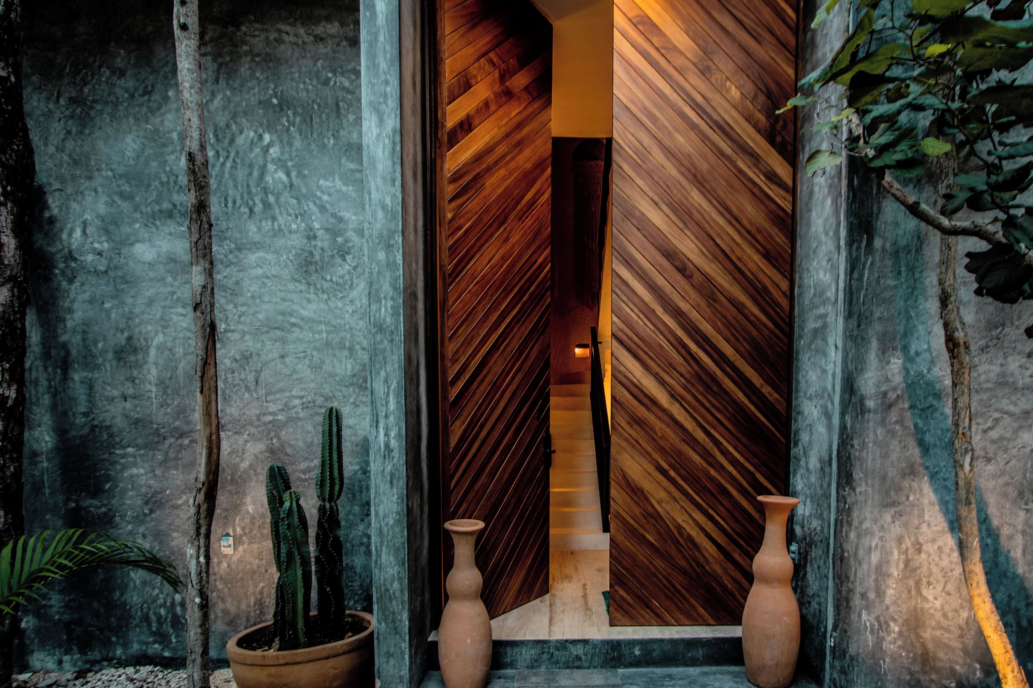 Una escalera de madera que conduce a una habitación de diseño moderno, flanqueada por jarrones grandes y una planta de cactus.