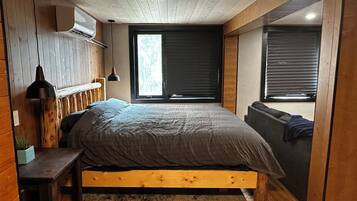 A bedroom with a wooden bed frame, a bedside table, a hanging lamp, and a window with blinds.