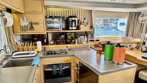 Une petite cuisine équipée d’un évier, d’une cuisinière, d’une machine à café et d’un four grille-pain. On trouve deux thermos et une bouteille de spiritueux sur le comptoir.