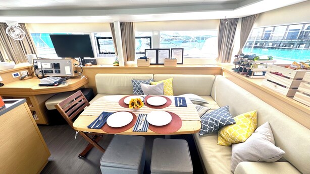 Un coin repas avec une table dressée pour deux personnes, un canapé et une vue sur la mer grâce à de grandes fenêtres.
