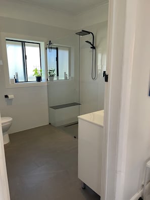 A modern bathroom with a toilet, a shower, a sink, and a window with plants.