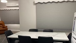 Un salón de conferencias con una mesa de mármol, sillas negras, un armario blanco y una ventana con persianas.