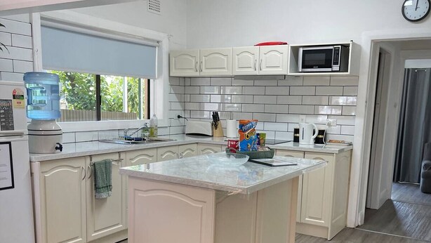 Una cocina moderna con armarios blancos, una isla central, un dispensador de agua y un microondas.