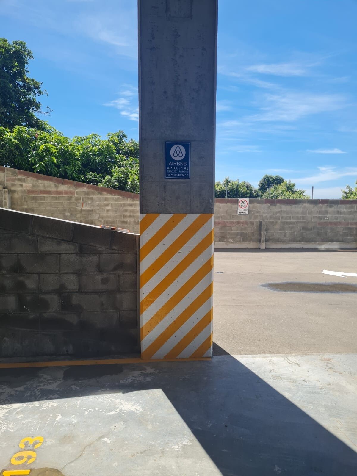 Un pilastro in cemento con un cartello blu che indica una proprietà Airbnb, un segnale di limite di velocità di 20 km/h e una barriera di sicurezza giallo e bianca.
