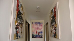 Een gang met aan beide kanten twee deuren, een plafondlamp en een schilderij aan de muur.