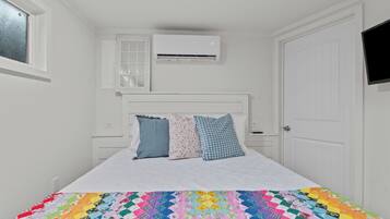 Ein Schlafzimmer mit einem Bett, weißen Wänden, einem Fenster, einer Klimaanlage und einer Tür.