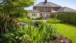 Une maison avec une façade en briques, un toit en tuiles et un jardin bien entretenu, agrémenté de diverses plantes et d’une pelouse.
