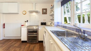 Une cuisine avec des meubles blancs, une cuisinière, un four et un lave-vaisselle. Une fenêtre offre une vue sur la verdure à l’extérieur.